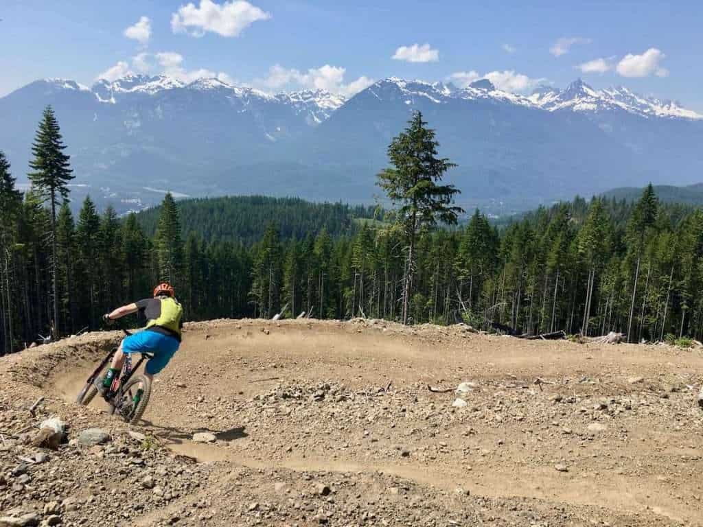 Mountain biker riding down big bermed turn on singletrack trail in Squamish, British Columbia with snow-capped peaks in the distance