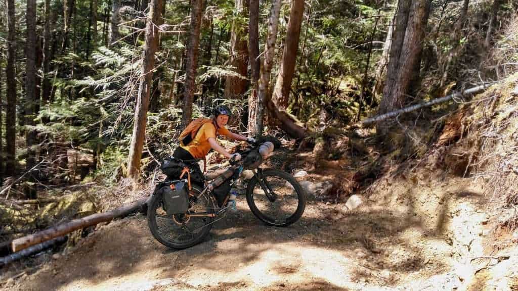 Becky pushing fully loaded bikepacking bike up steep switchback in Washington