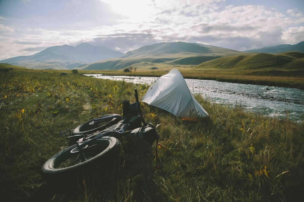 Tent set up by river with bike lying next to it in remote part of Kyrgyzstan