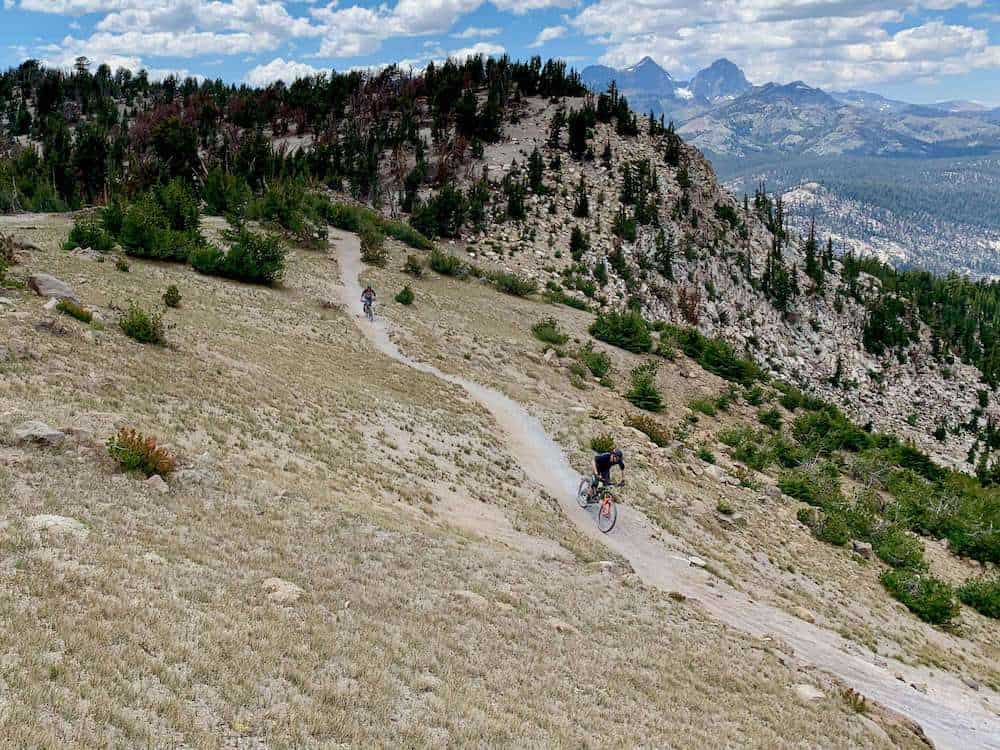 Mountain bikers on singletrack trail at Mammoth Bike Park in California with tall mountain range in distance