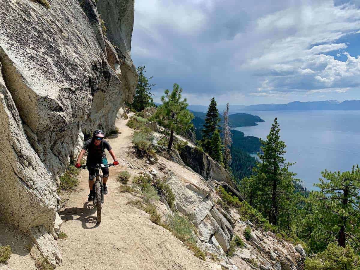 Mountain biker on Tahoe Flume trail with rock cliff on one side and drop off on the other with Lake Tahoe in the background