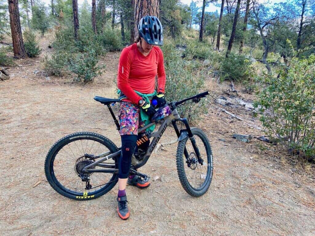Female mountain biker stopped on trail opening top tube bag for a snack