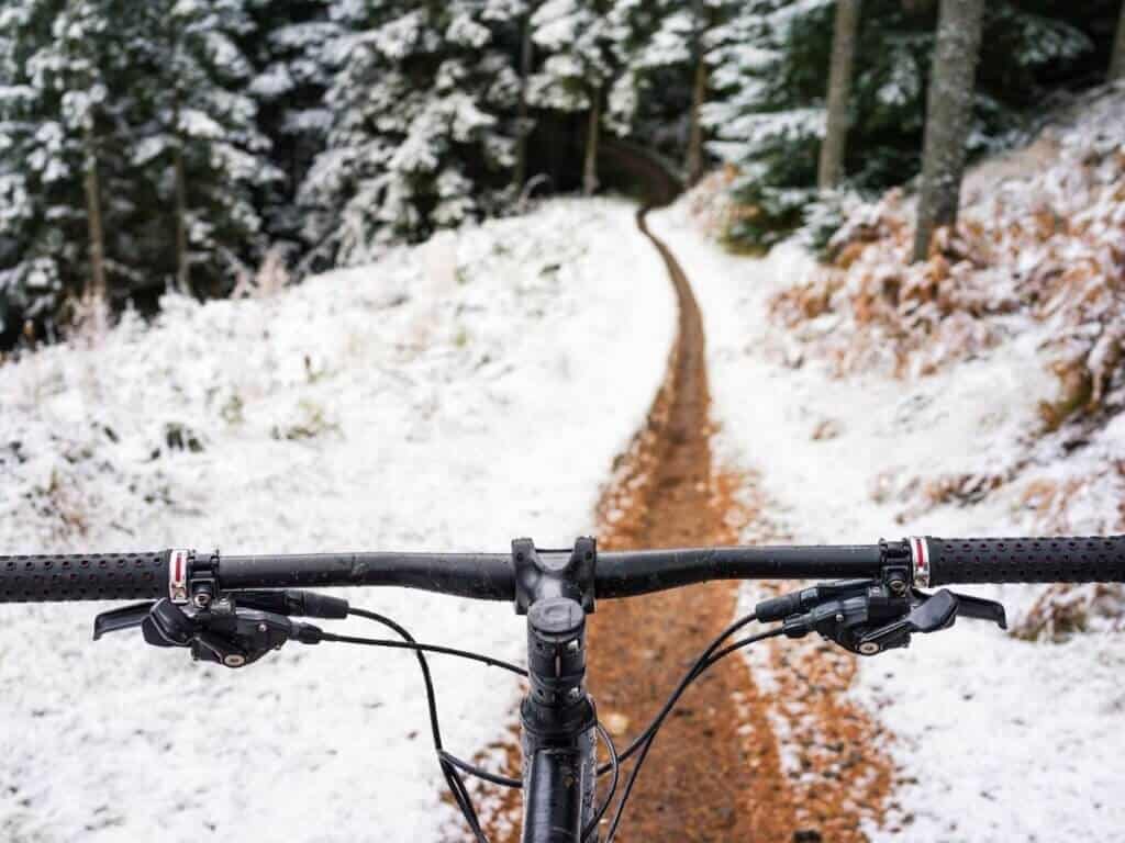 Photo out over front of mountain bike handlebars of trail in winter lined with snow