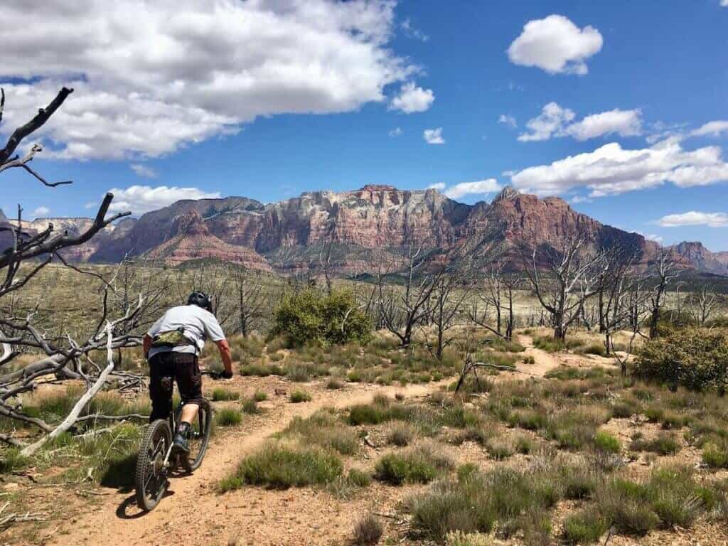 Mountain biker riding along desert singletrack trail in Hurricane, Utah with red rock mountains in distance