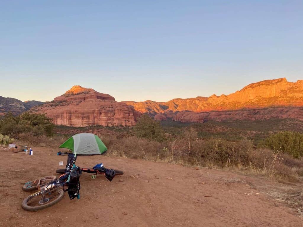 Sun casting glow over red rock cliffs above dispersed campsite outside of Sedona, Arizona