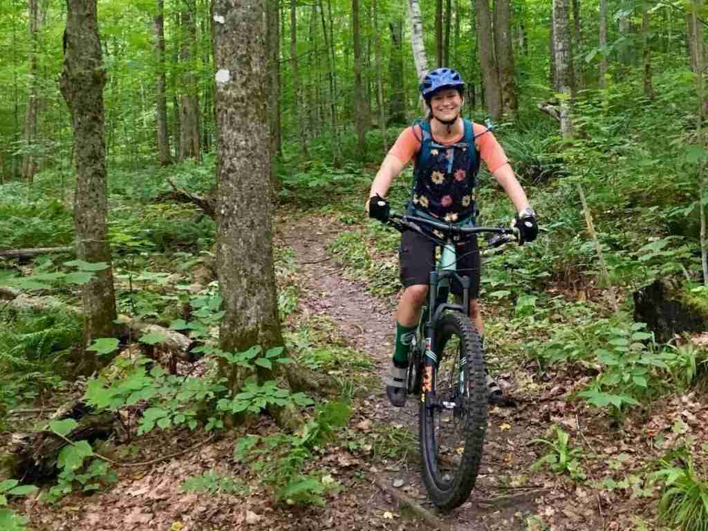 mountain biker smiling for camera while pedaling down forested trail in Vermont