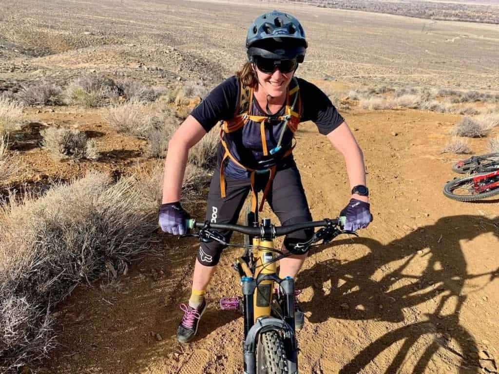 Becky sitting on mountain bike with foot on the ground and smiling at camera on dirt hill in California