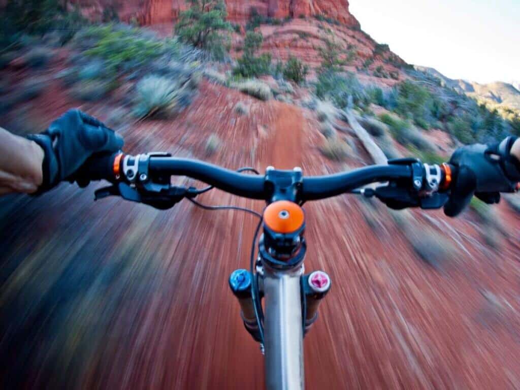 Photo out over mountain bike handlebars while rider is biking over red dirt trail