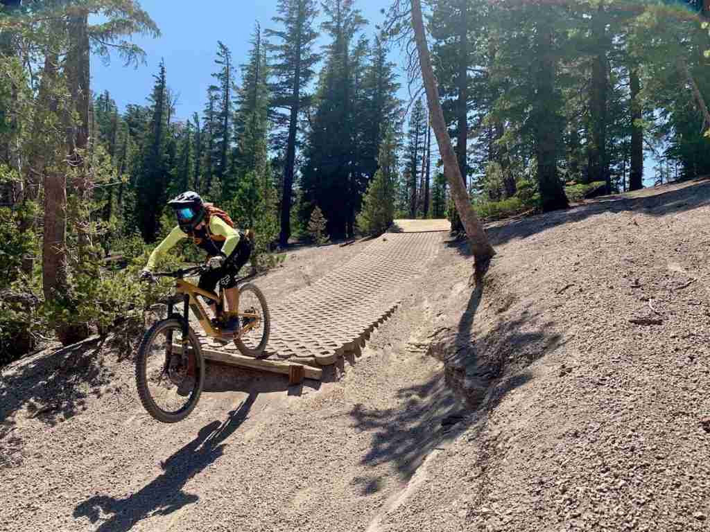 Woman riding mountain bike off ramp at Mammoth Mountain Bike Park in California