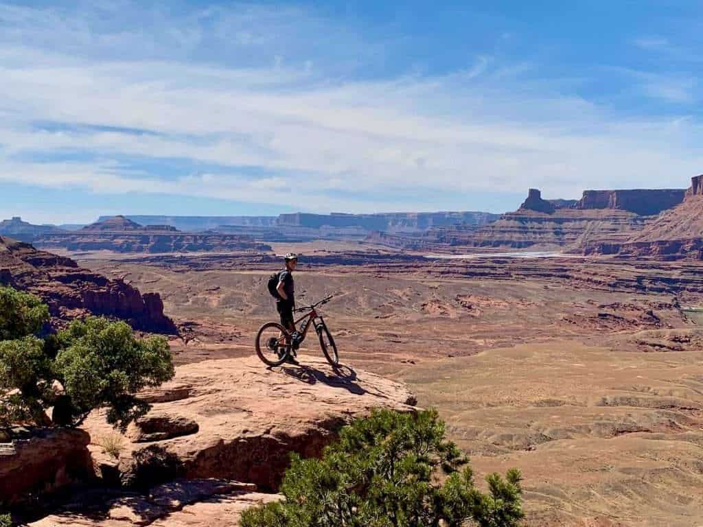 Mountain biker standing next to bike on exposed rock ledge in Utah with red rock canyonland views as backdrop