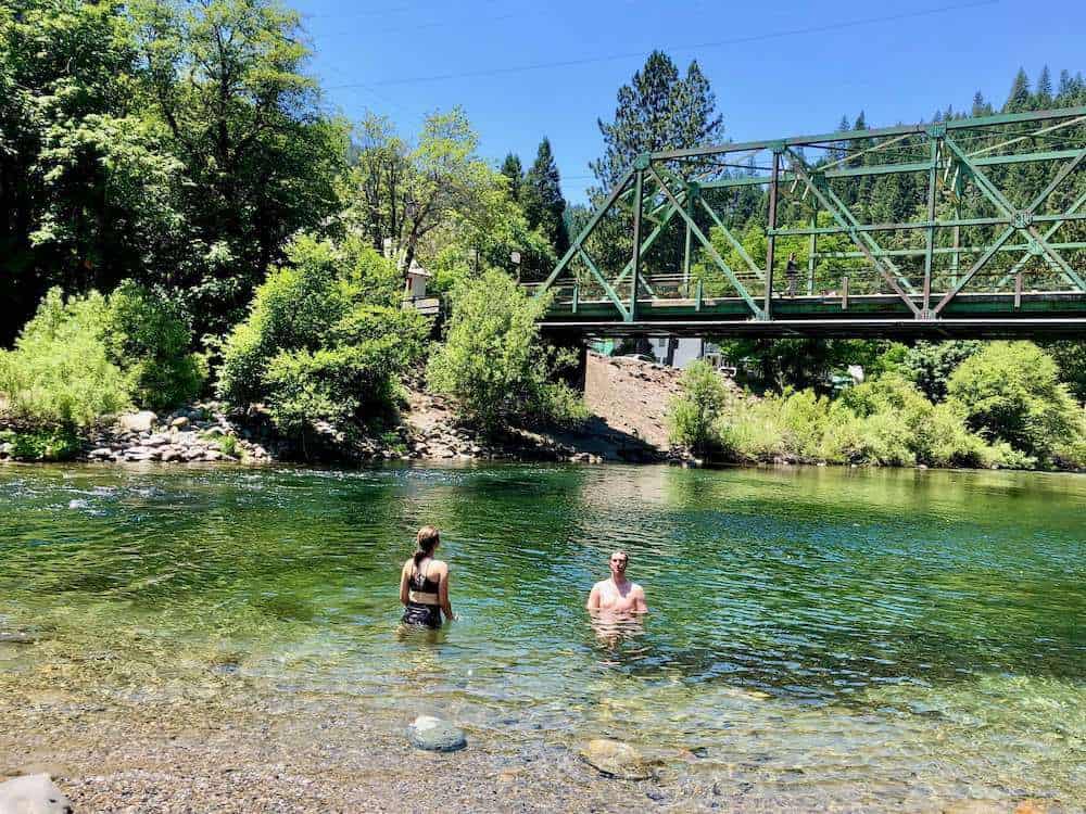 Two people swimming in clear river with bridge overhead