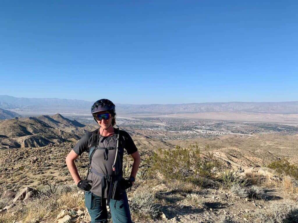 Becky wearing mountain bike apparel posing for photo in front of vast mountainous desert landscape in California