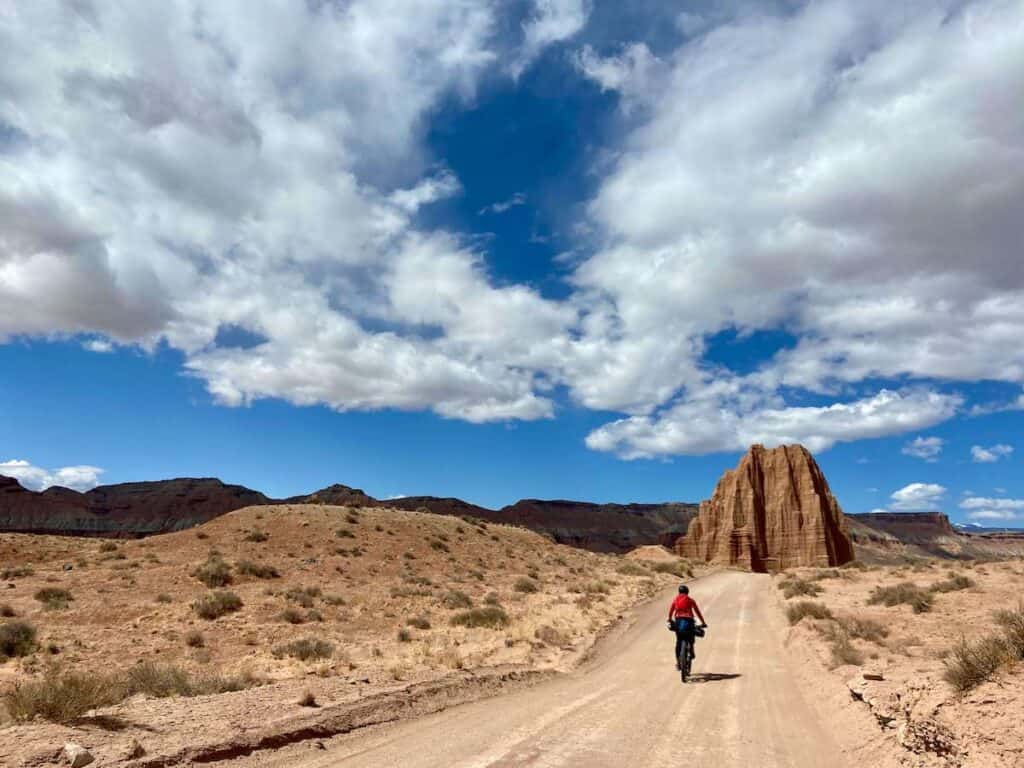 Woman riding loaded bikepacking bike on remote road in Cathedral Valley in Capitol Reef National Park with tall sandstone monolith in front of her