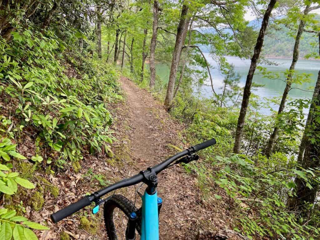 Photo out over front of mountain bike handlebars onto singletrack trail next to lake in North Carolina