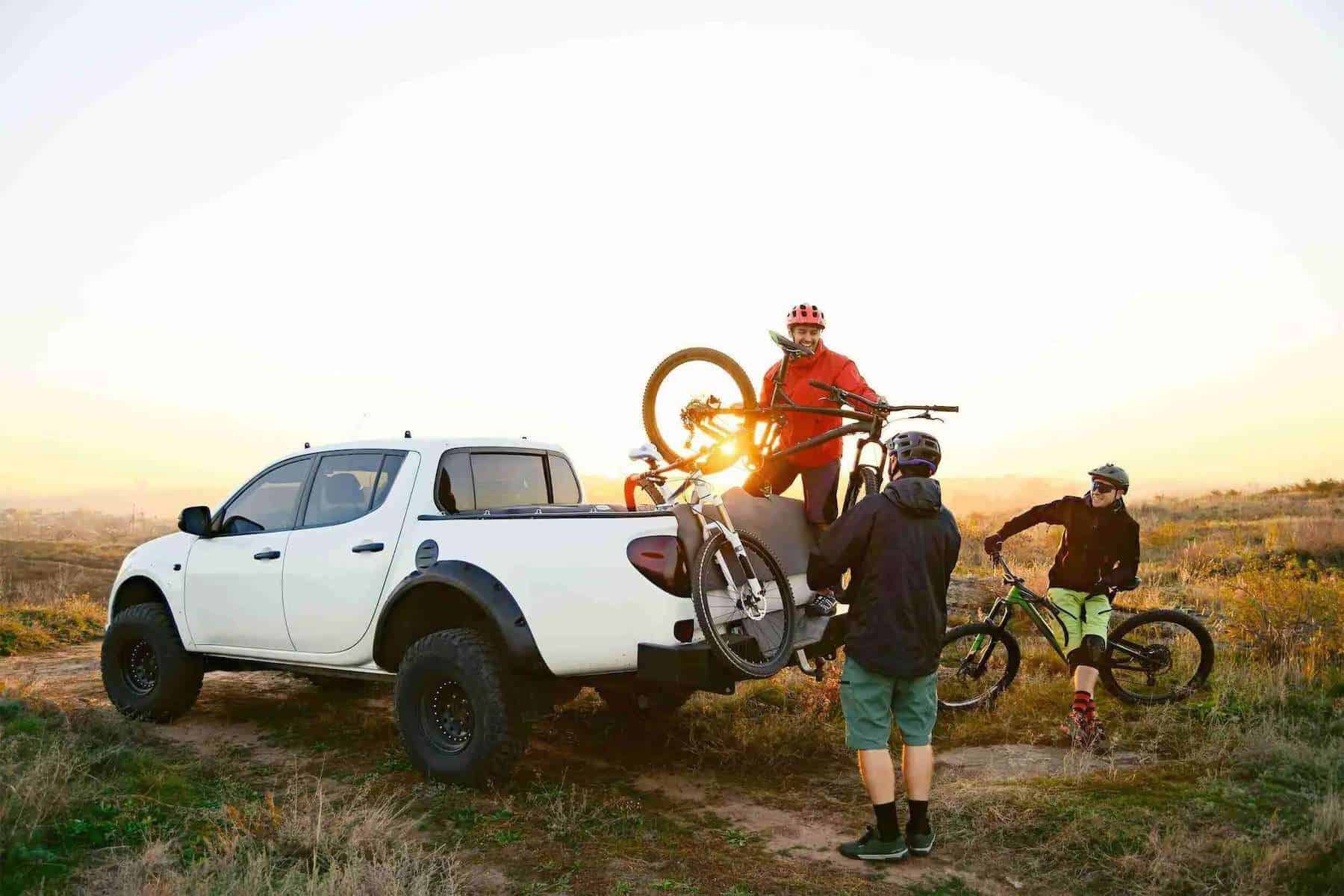 Three mountain bikers loading bikes into bed of pick-up truck fitted with tailgate bike pad