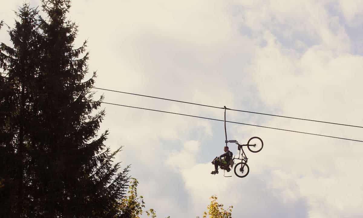Man sitting on chairlift with mountain bike on rack behind him