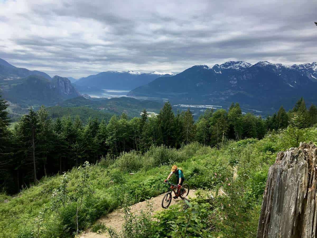 Mountain biker climbing up singletrack trail in Squamish, British Columbia with mountain and fjord landscape in background