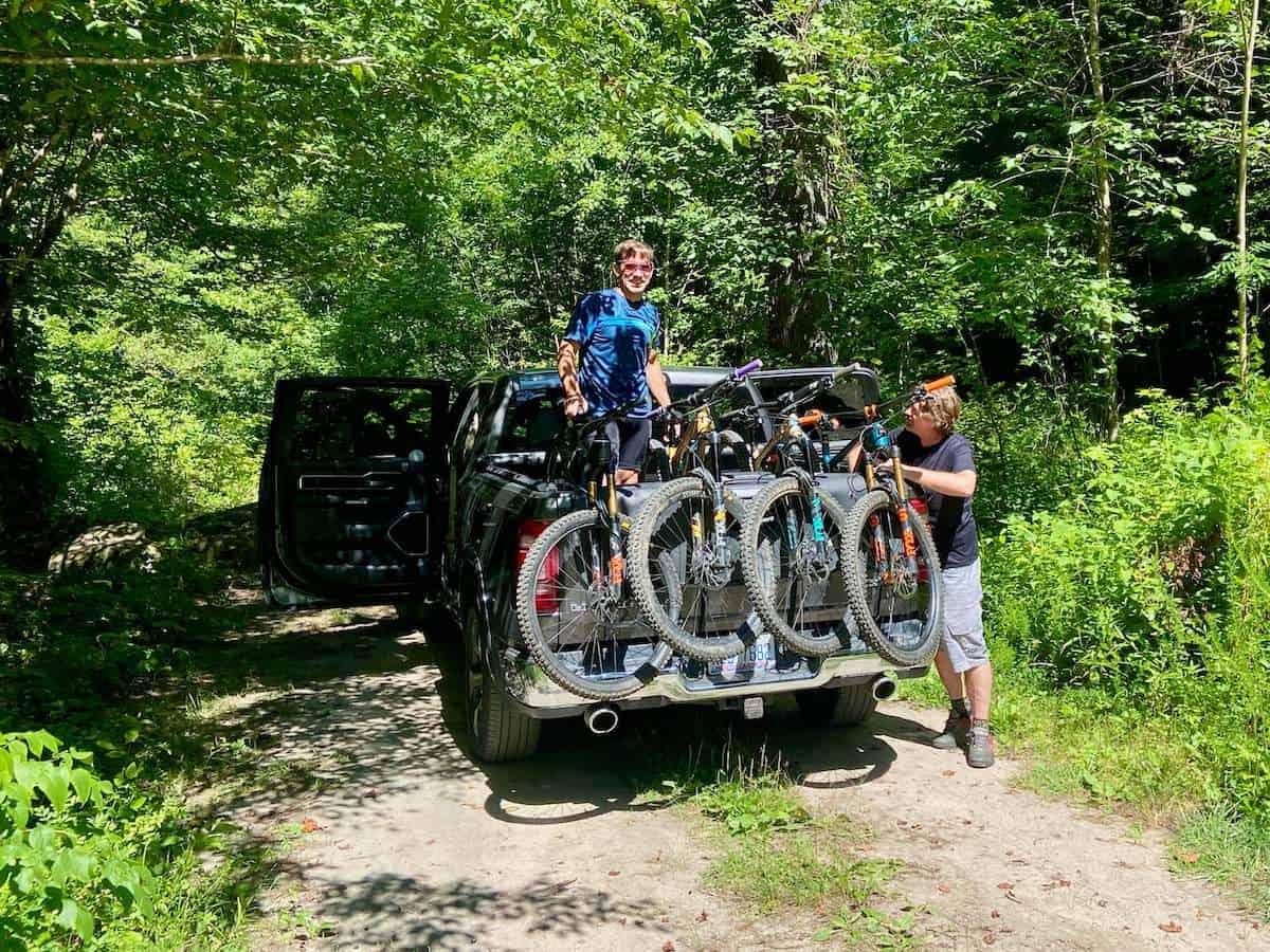 Two men loading mountain bikes into back of pickup truck fitted with a tailgate bike pad