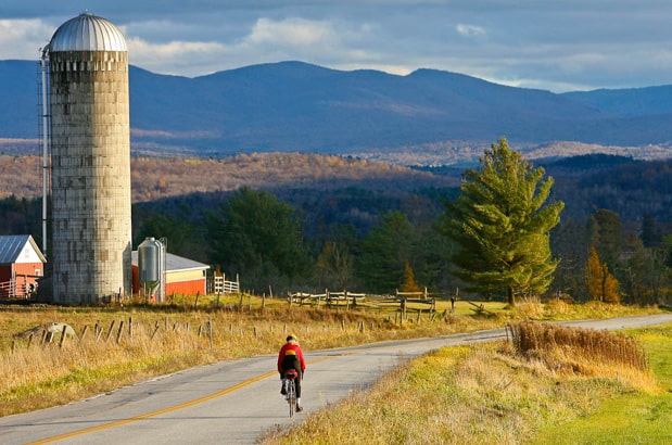 Cyclist on paved backroad in Vermont with mountains in the distance and farm silo off to the left