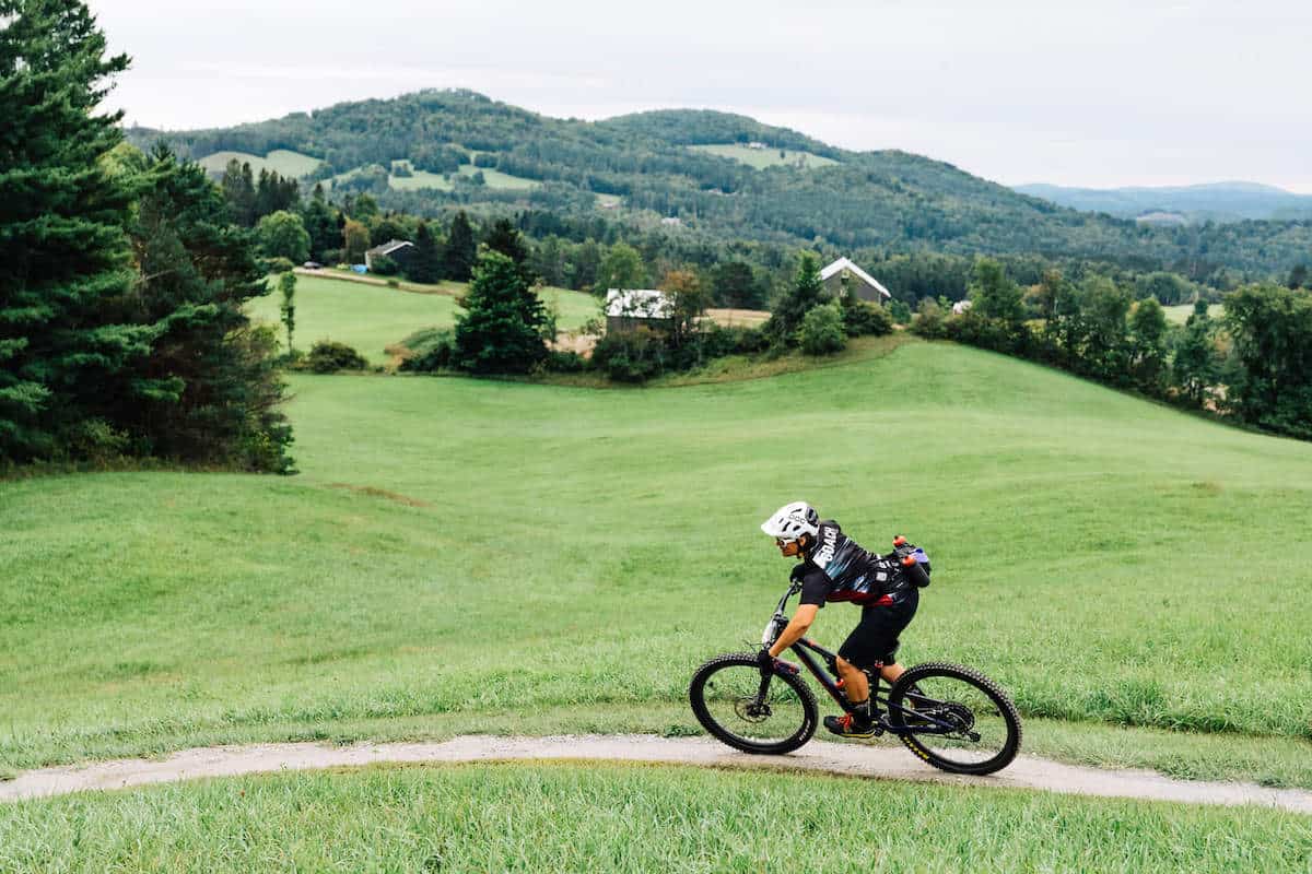 Mountain biker riding on trail at Kingdom Trails in Vermont with pasture and mountains in background