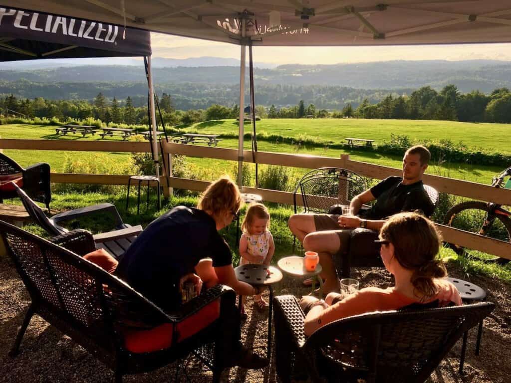 Group of people sitting around tables under tent at Kingdom Trails with beautiful view out over rolling hills and pasture