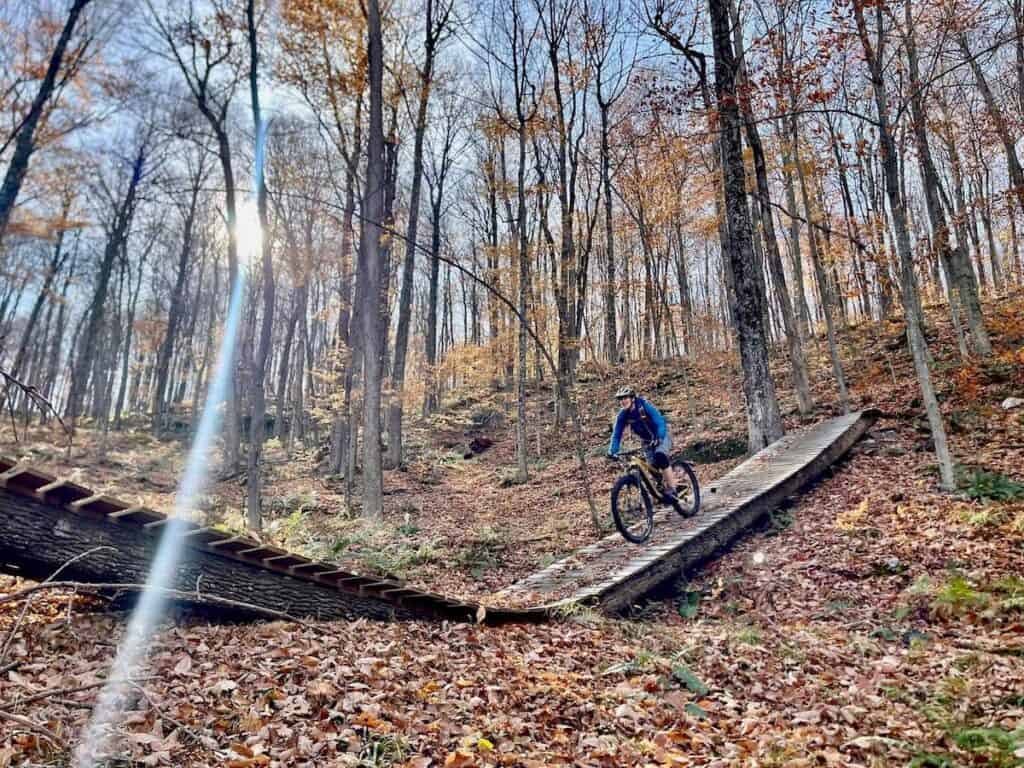 Mountain biker riding down long wooden ramp in the woods in Vermont in late fall