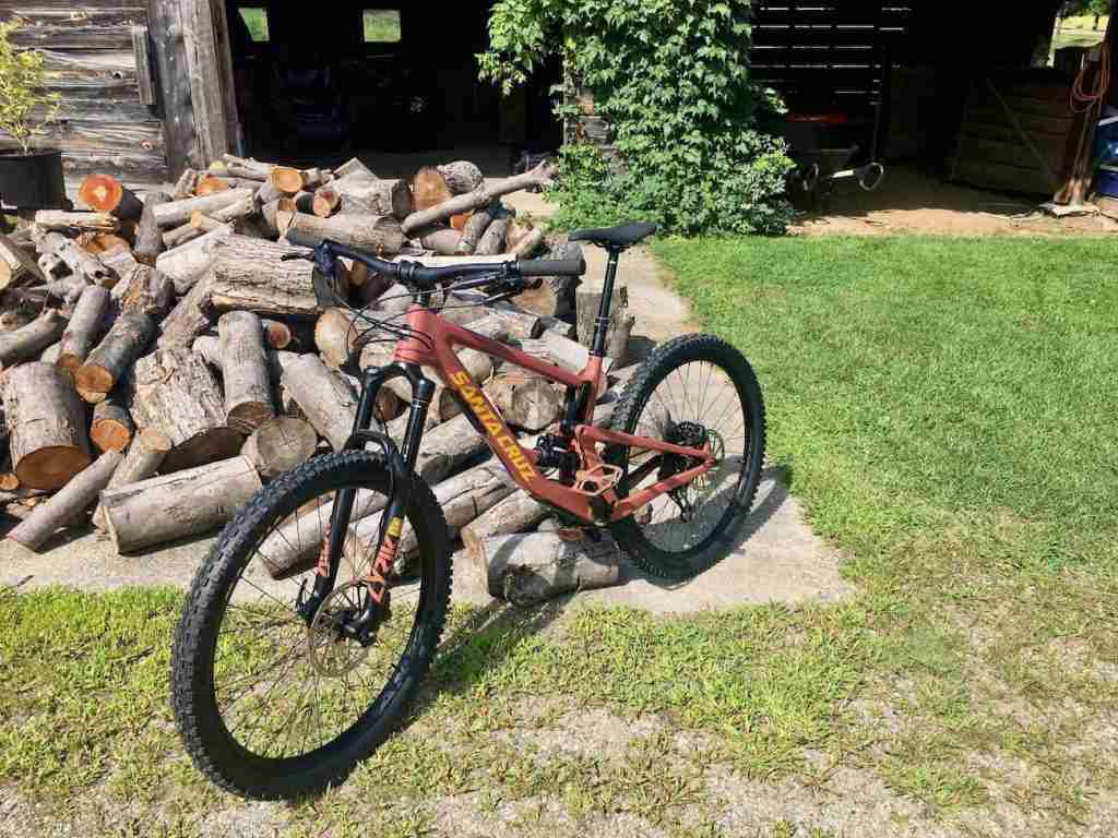 Santa Cruz Bronson mountain bike leaning against woodpile in front of garage