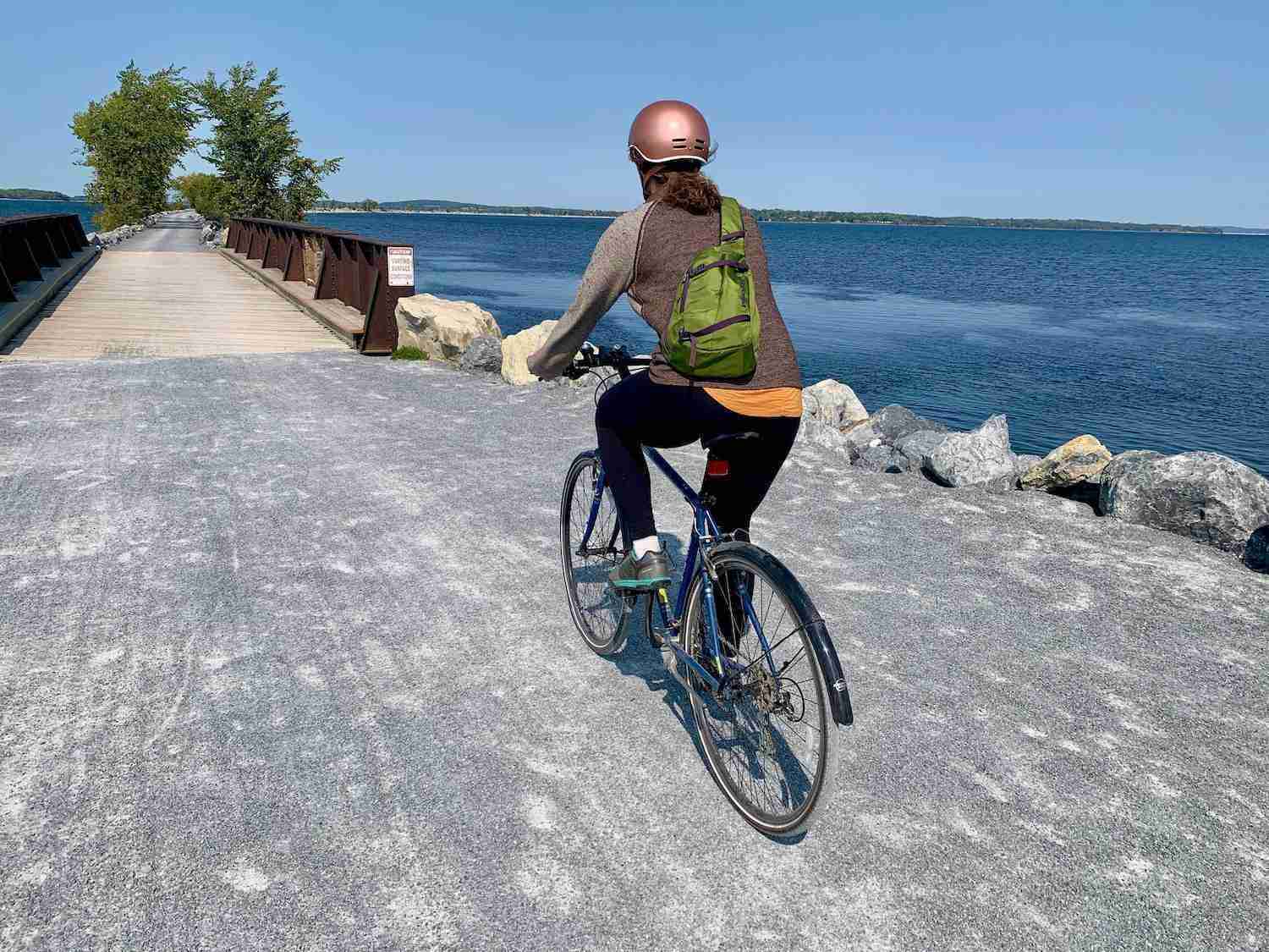 Woman riding bike on gravel causeway bike path in Vermont with Lake Champlain on right side side