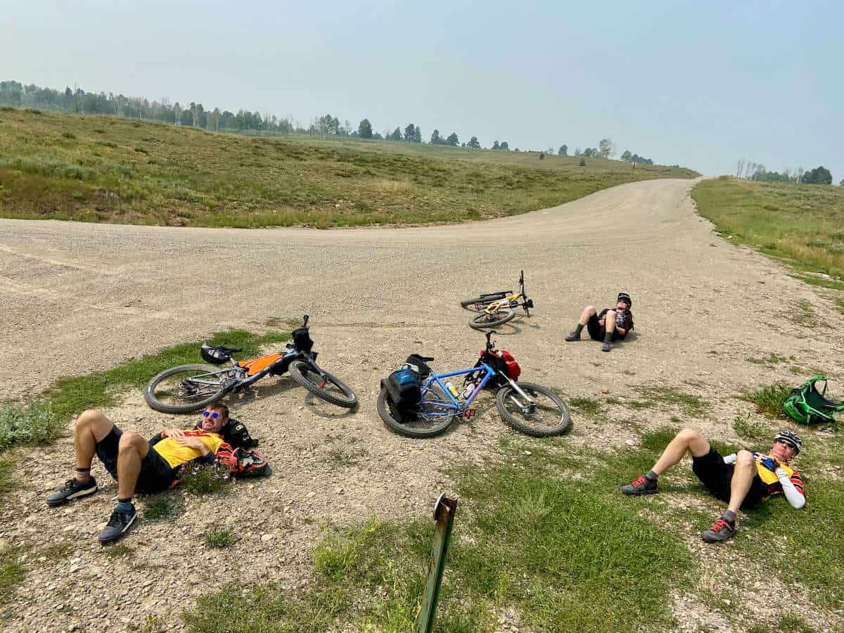 Mountain bikers taking a break and lying on their backs next to bikes on dirt road on the Telluride to Moab mountain bike ride