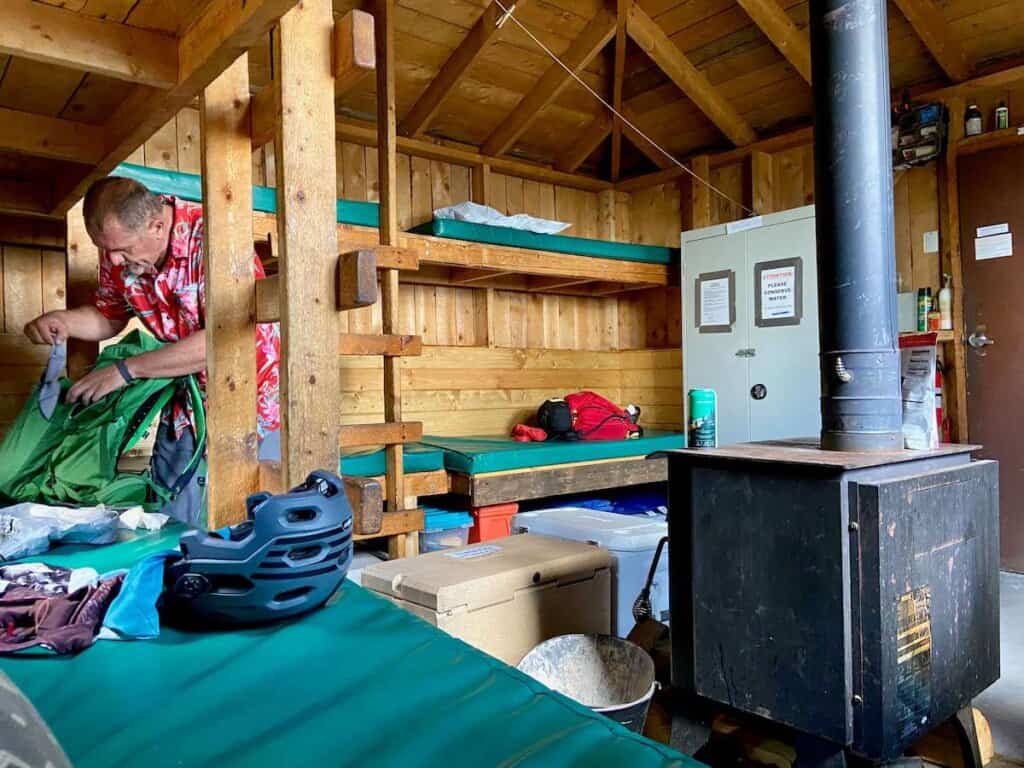 Inside of San Juan Huts System hut with bunkbeds and vinyl matresses, wood stove, and coolers