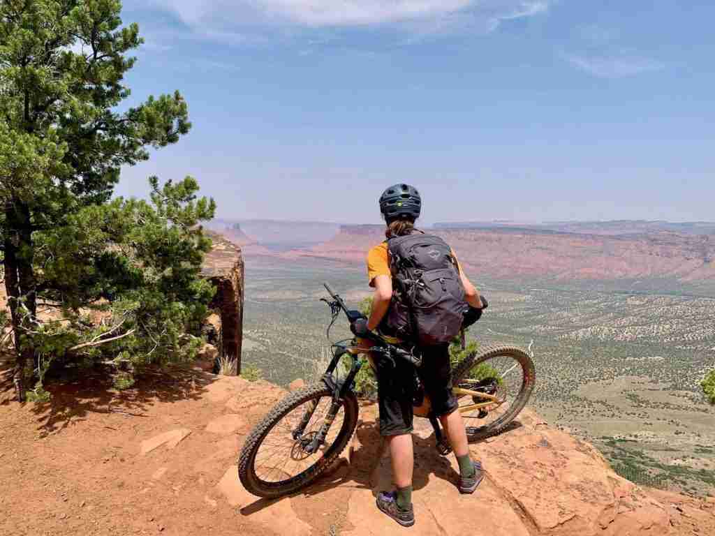 Woman standing with bike looking out over Utah vista wearing Osprey Mira backpack