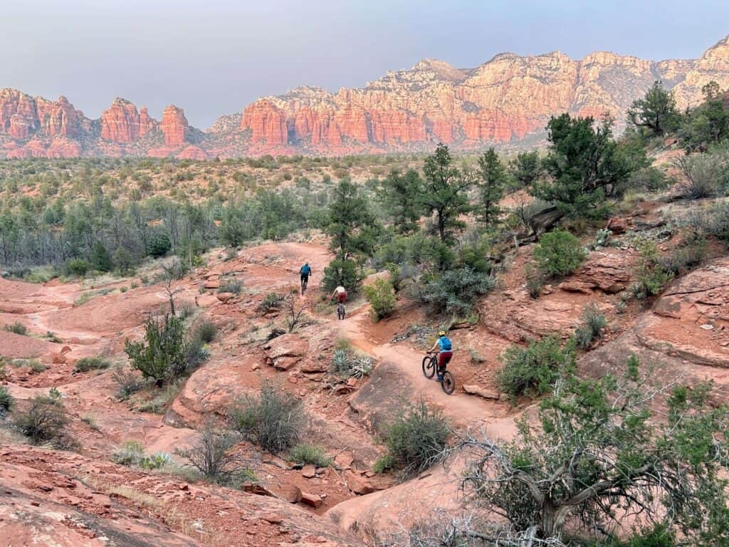 Mountain bikers riding on trail in Sedona with stunning red rock bluffs in the distance