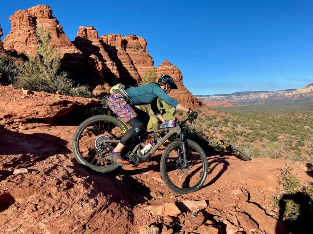 Female mountain biker riding bike down steep red rock section on trail in Sedona