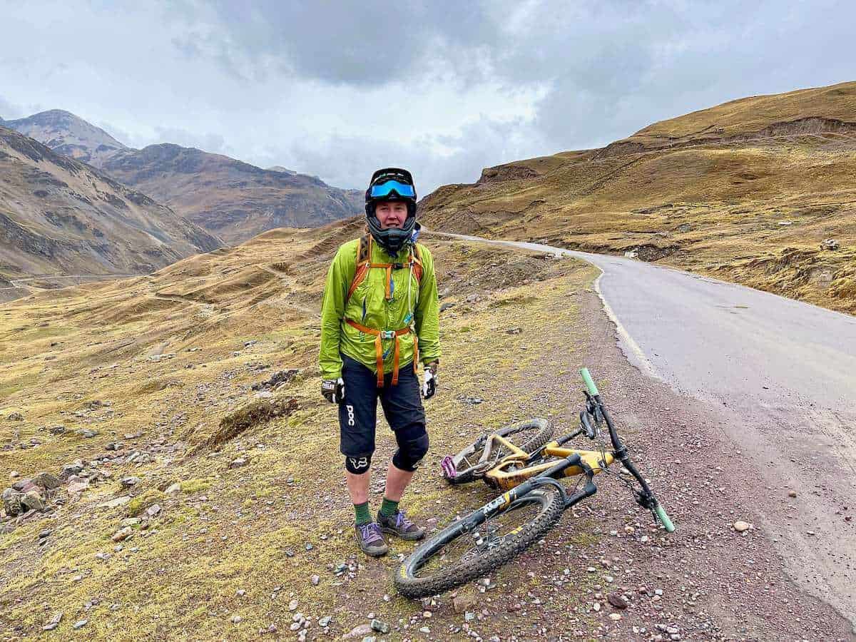Mountain biker standing on side of remote road in Peru with bike on ground wearing full face helmet