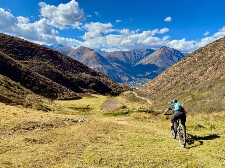 Mountain biker riding bike down grassy trail in valley in Sacred Valley of Peru