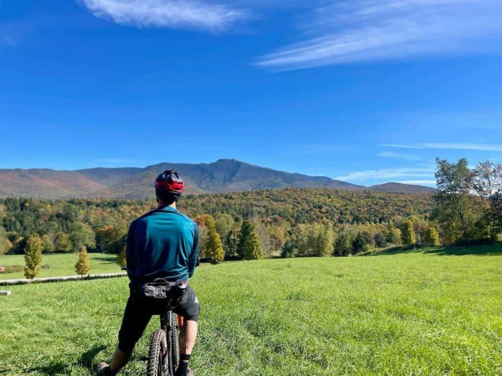 Mountain biker looking out over Vermont fields and Mt. Mansfield from grassy trail