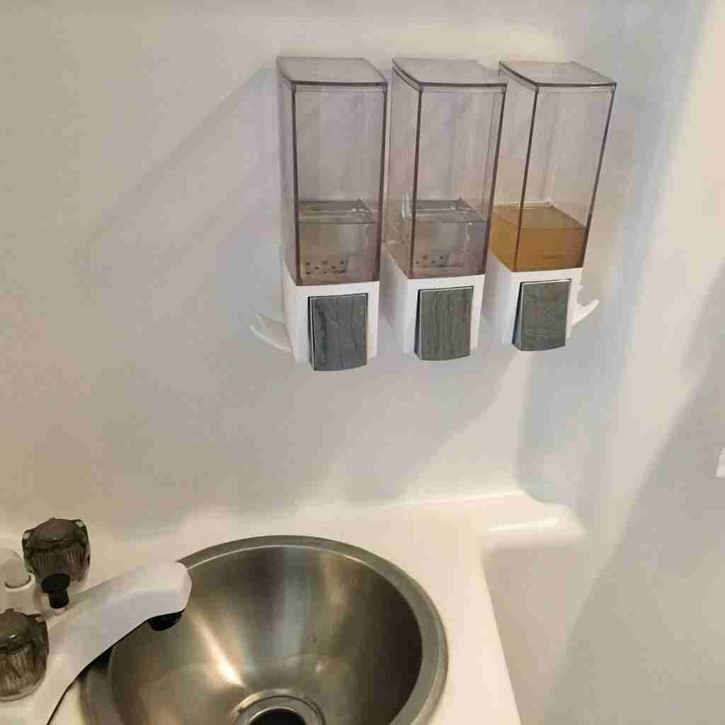 Triple liquid dispenser attached to bathroom wall over small sink in camper van