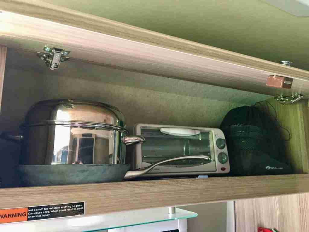 Pots and toaster oven in overhead cabinet in camper van