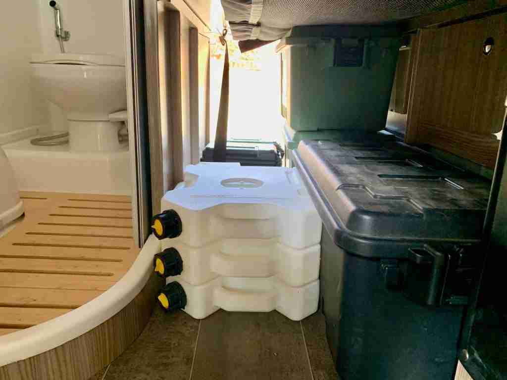 Storage for water jugs and gear beneath bed of converted campervan 