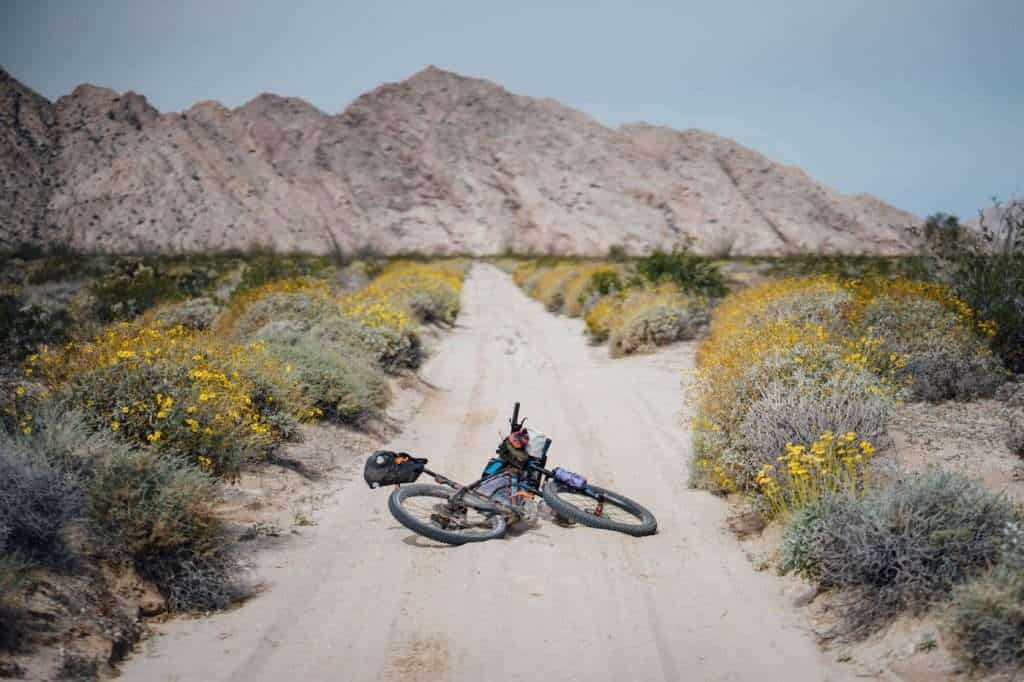 Loaded bikepacking bike laying down in middle of sandy stretch of road in desert landscape of Arizona on the Camino del Diablo bikepacking route