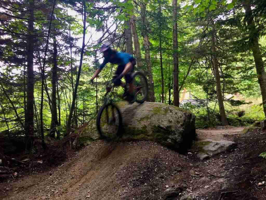 Blurry photo of mountain biker riding up rock and rolling down the other side