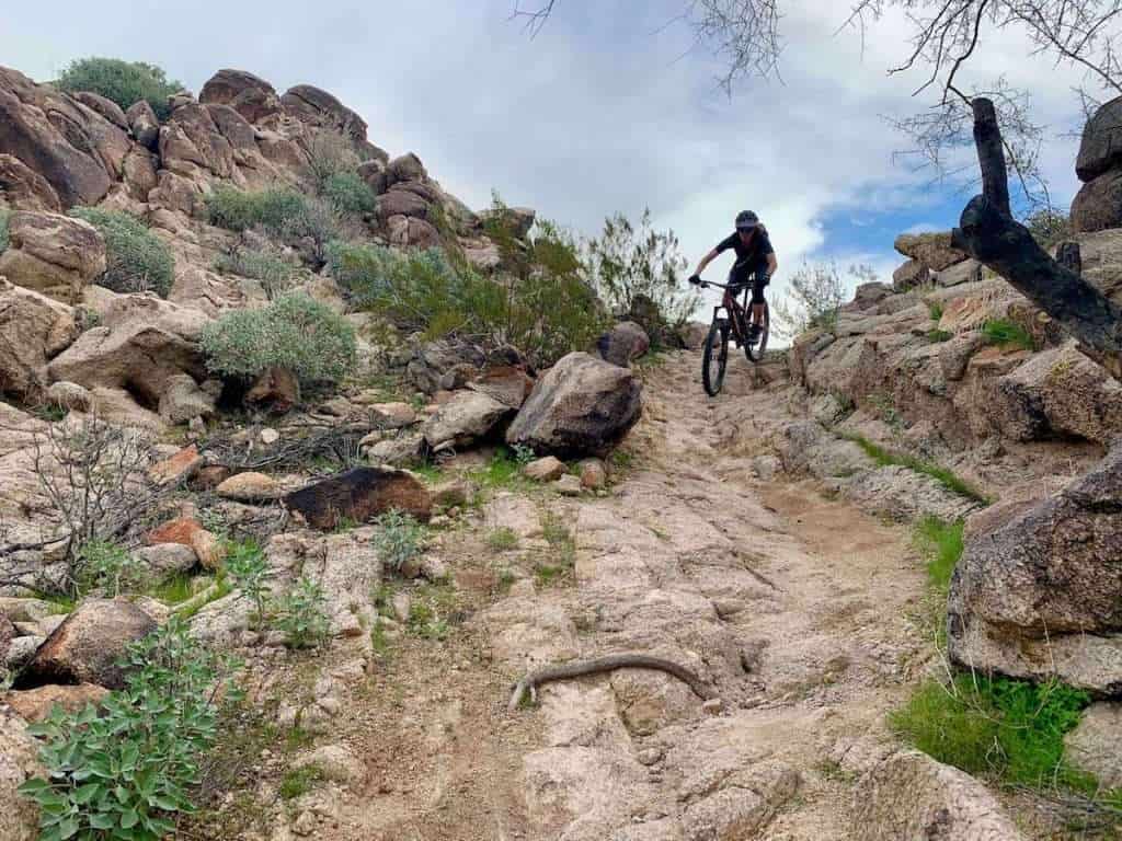 Mountain biker riding bike down narrow rocky shoot on trail in Phoenix, Arizona