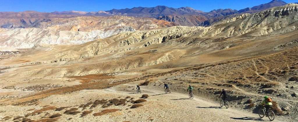 Mountain bikers riding down singletrack trail in high desert landscape of Nepal