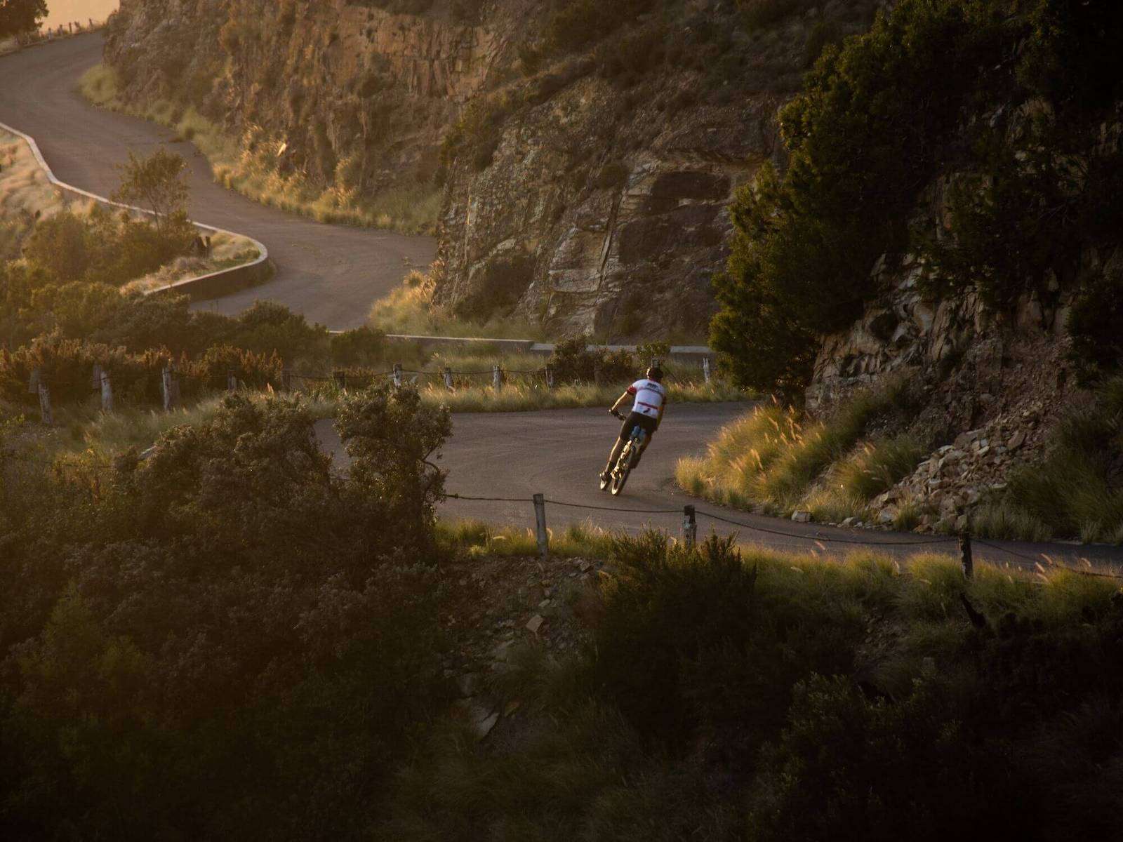 Road cyclist on empty, winding road with golden sunlight of sunset