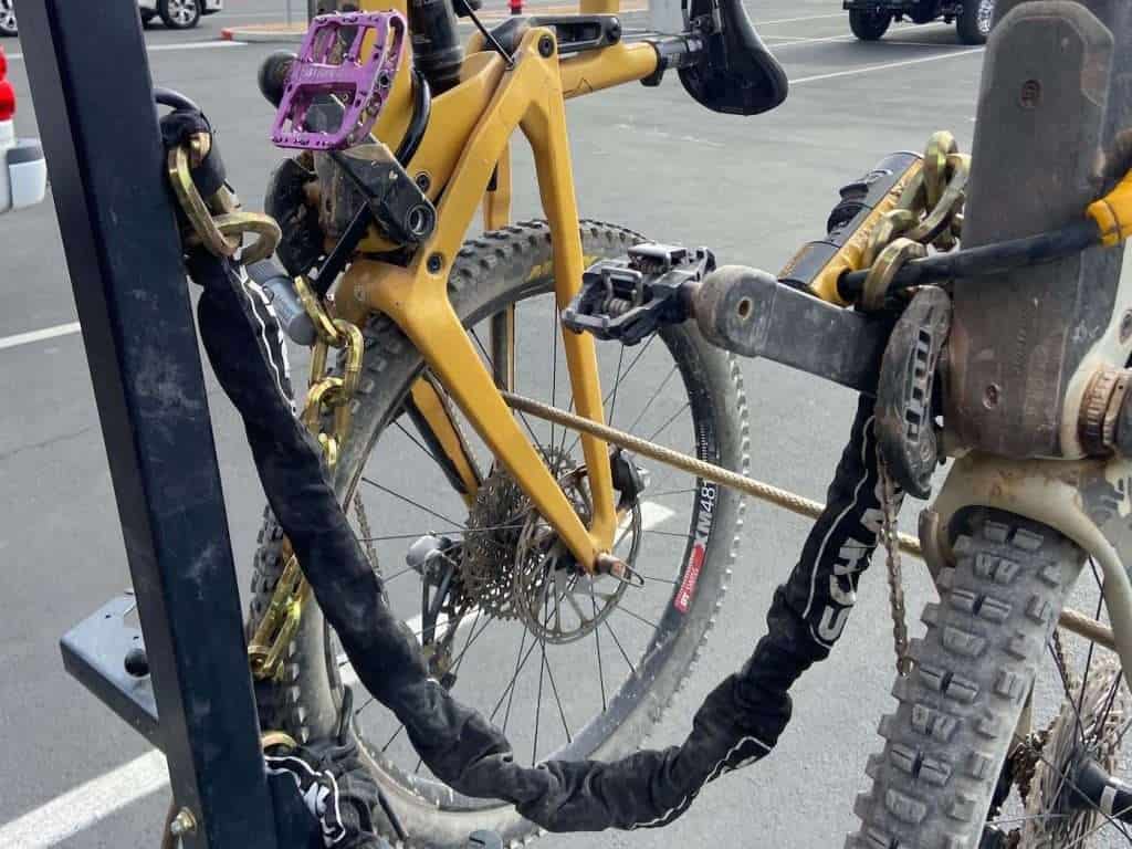 Two mountain bikes on a hanging bike rack secured by three different types of locks: a cable lock, two burly chain locks, and a u-shaped lock