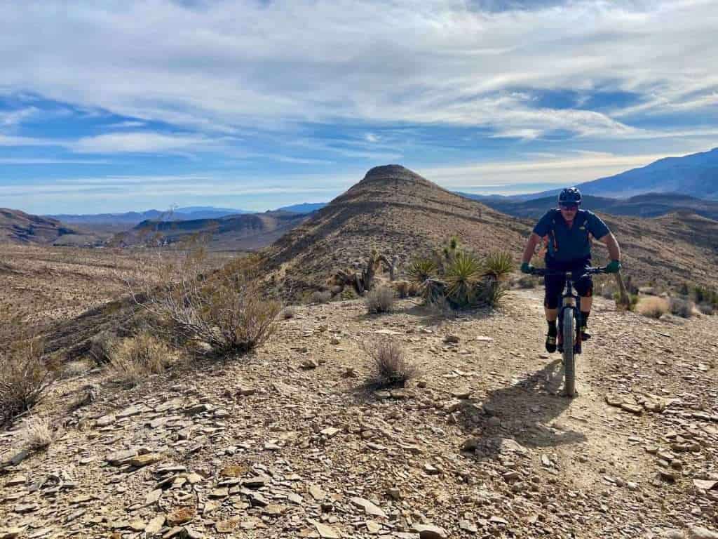 Male mountain biker finishing climb on trail outside Las Vegas, Nevada with mountains in the background