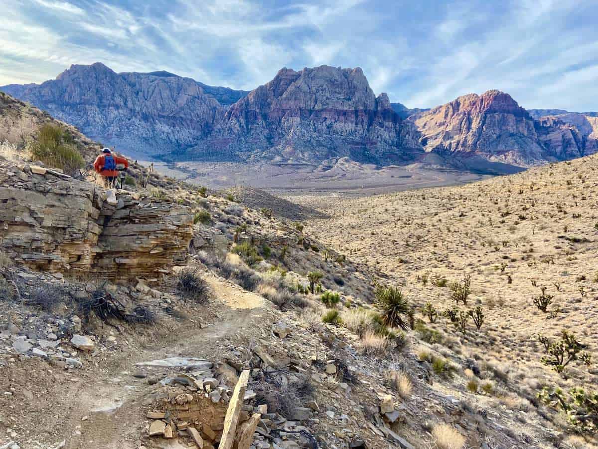 Man riding bike on desert mountain bike trail outside of Las Vegas, Nevada with tall rock bluffs in distance