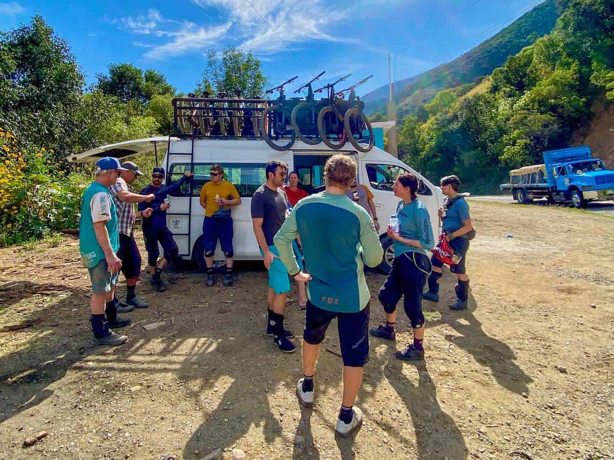 Mountain bikers standing around van at end of ride drinking beverages with bikes loaded on top of van