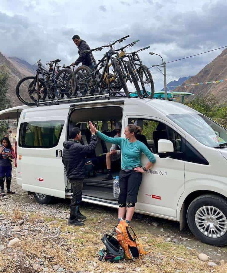 Mountain bikers high-fiving at the end of trail. Van with bikes on top in background