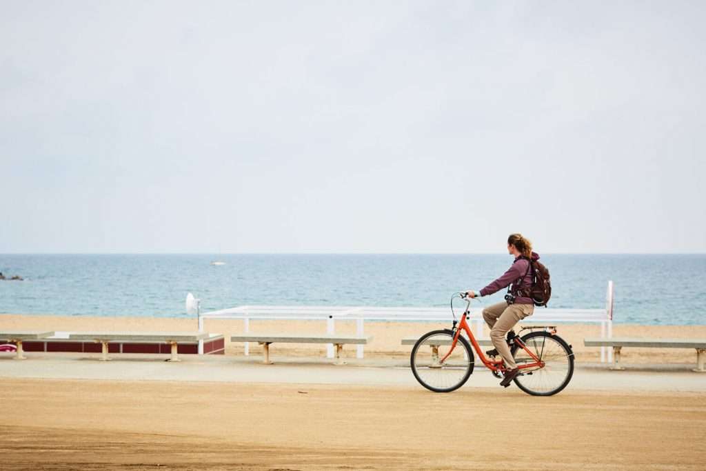 Female riding beach cruiser bike along ocean front path in Barcelona, Spain